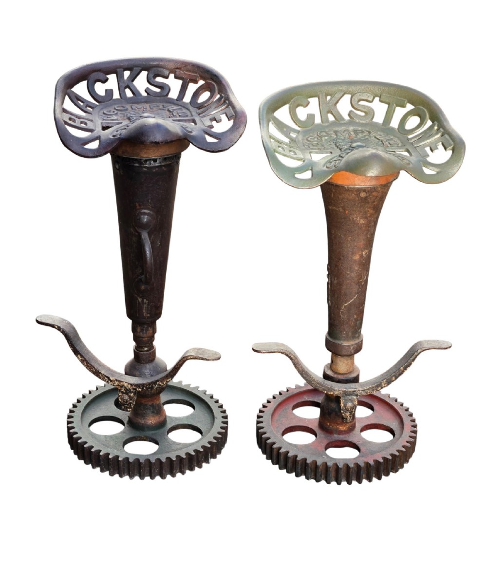 A pair of heavy industrial bar stools constructed with embossed Blackstone and Company cast-iron tractor seats, central metal columns with integrated footrests, and heavy gear cog bases. View V