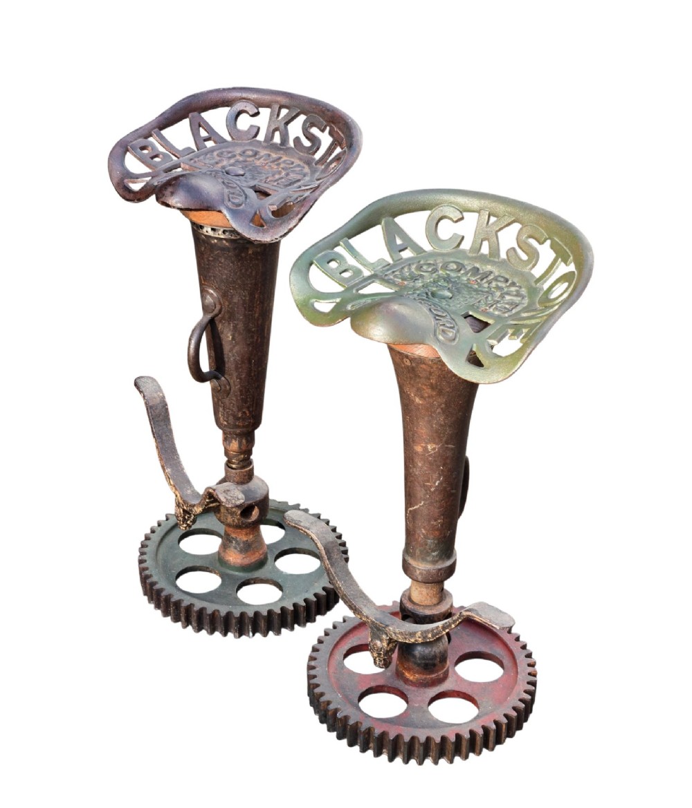 A pair of heavy industrial bar stools constructed with embossed Blackstone and Company cast-iron tractor seats, central metal columns with integrated footrests, and heavy gear cog bases. View VI
