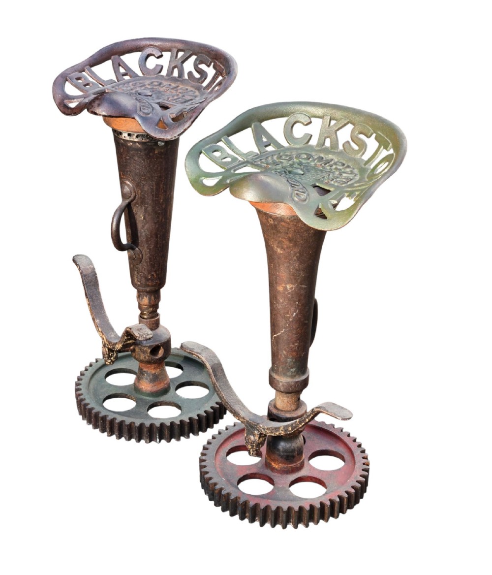 A pair of heavy industrial bar stools constructed with embossed Blackstone and Company cast-iron tractor seats, central metal columns with integrated footrests, and heavy gear cog bases. View VII