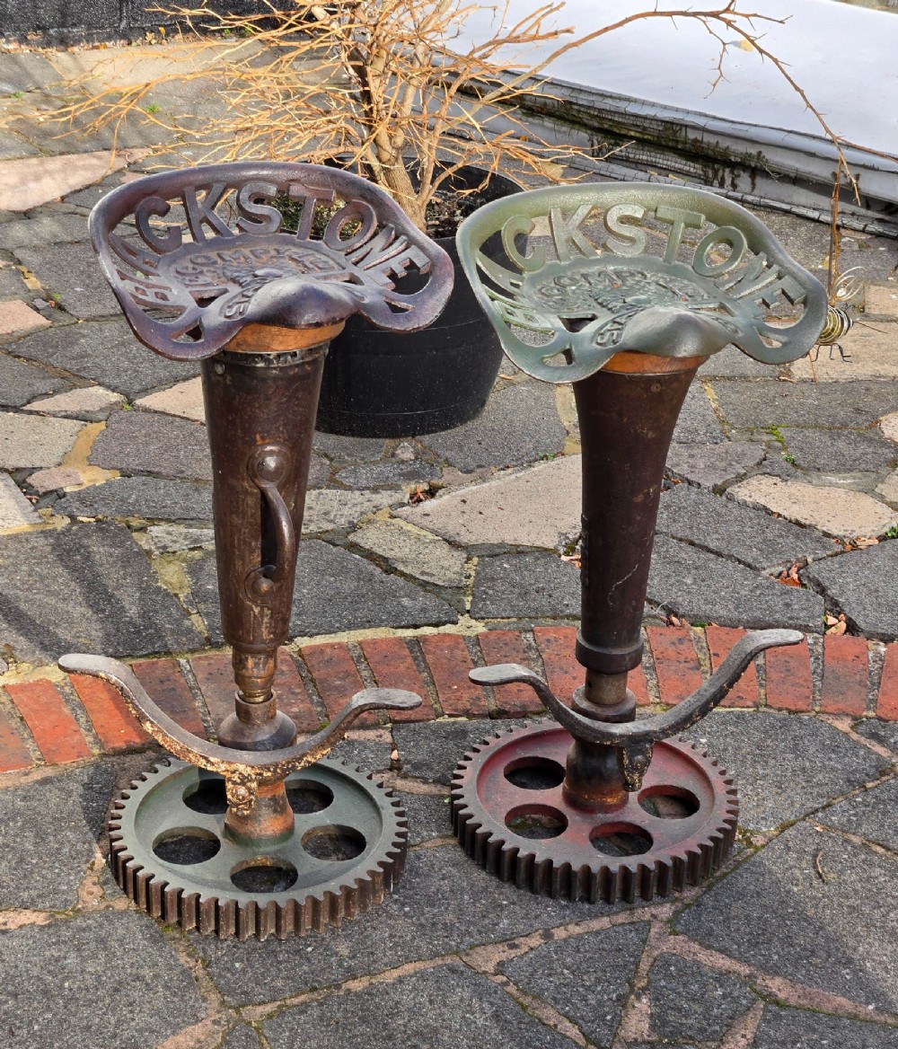 A pair of heavy industrial bar stools constructed with embossed Blackstone and Company cast-iron tractor seats, central metal columns with integrated footrests, and heavy gear cog bases. View XV