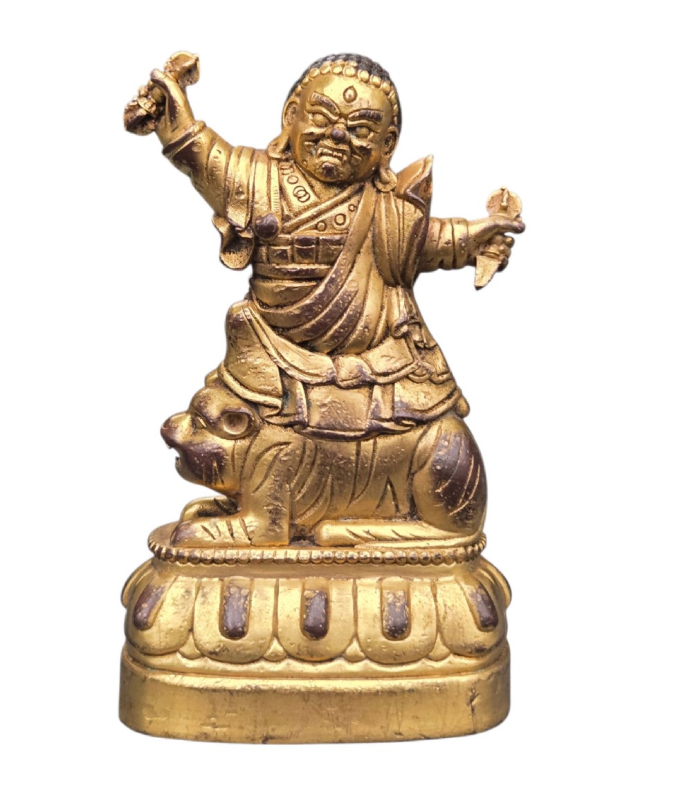 A sixteenth to seventeenth-century Sino-Tibetan gilt-bronze votive figure depicting a wrathful deity seated on a tiger atop a lotus pedestal. View IX