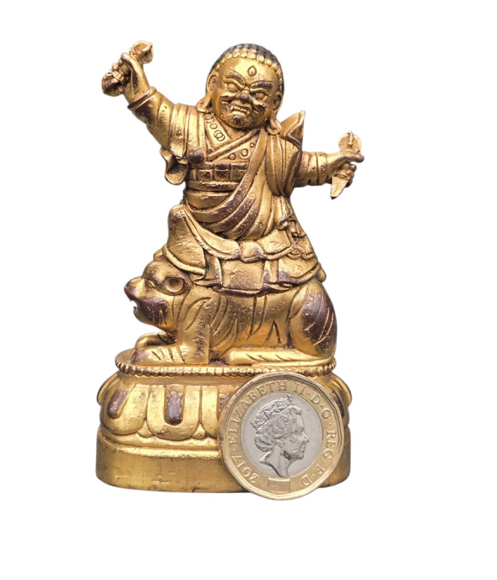 A sixteenth to seventeenth-century Sino-Tibetan gilt-bronze votive figure depicting a wrathful deity seated on a tiger atop a lotus pedestal. View X
