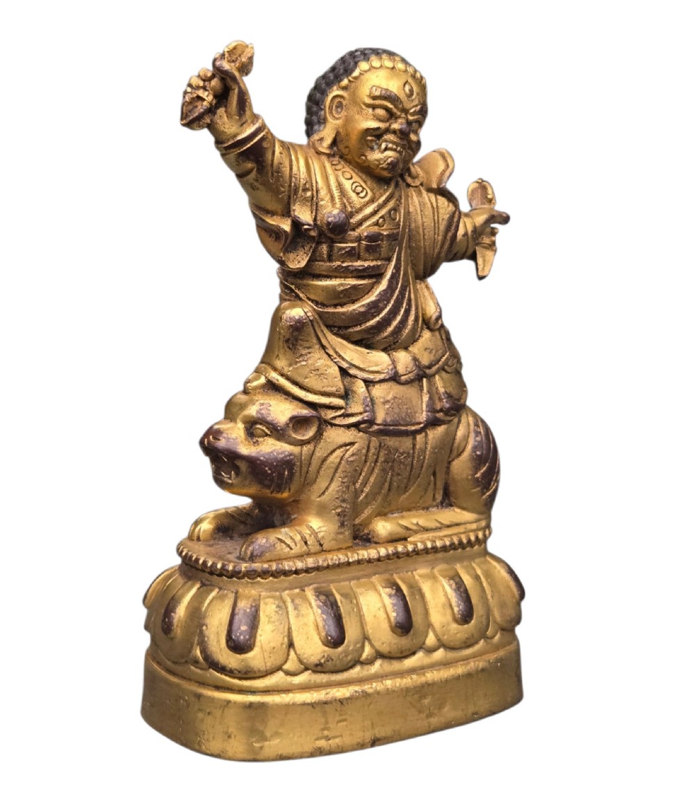 A sixteenth to seventeenth-century Sino-Tibetan gilt-bronze votive figure depicting a wrathful deity seated on a tiger atop a lotus pedestal. View XI