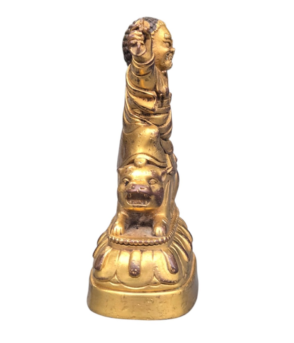 A sixteenth to seventeenth-century Sino-Tibetan gilt-bronze votive figure depicting a wrathful deity seated on a tiger atop a lotus pedestal. View XII