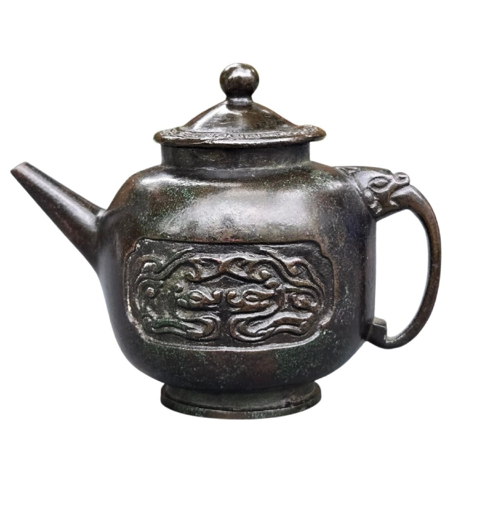 A dark patinated cast bronze vessel in ewer form featuring a dragon-head handle, a tapered spout, and carved relief panels.