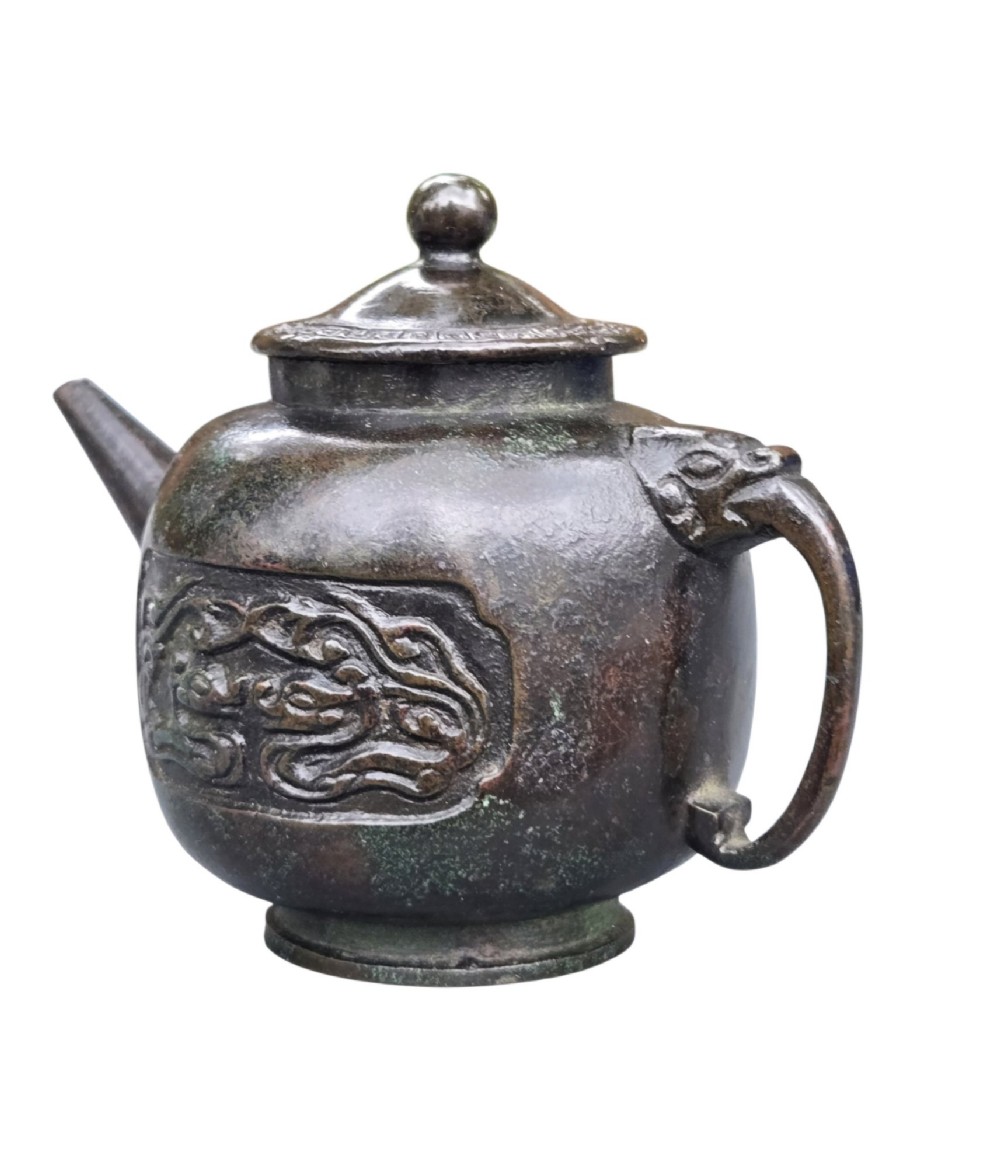 A dark patinated cast bronze vessel in ewer form featuring a dragon-head handle, a tapered spout, and carved relief panels. View II