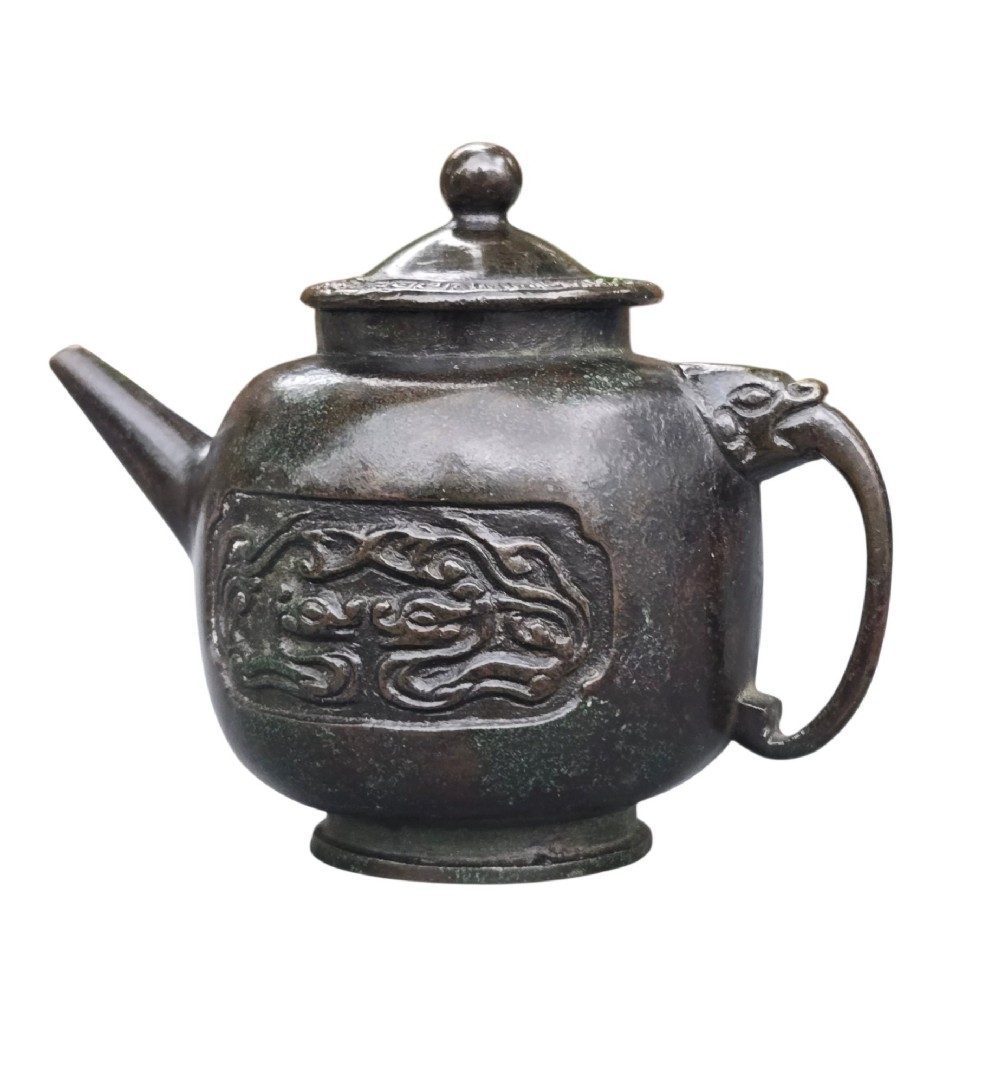 A dark patinated cast bronze vessel in ewer form featuring a dragon-head handle, a tapered spout, and carved relief panels. View III