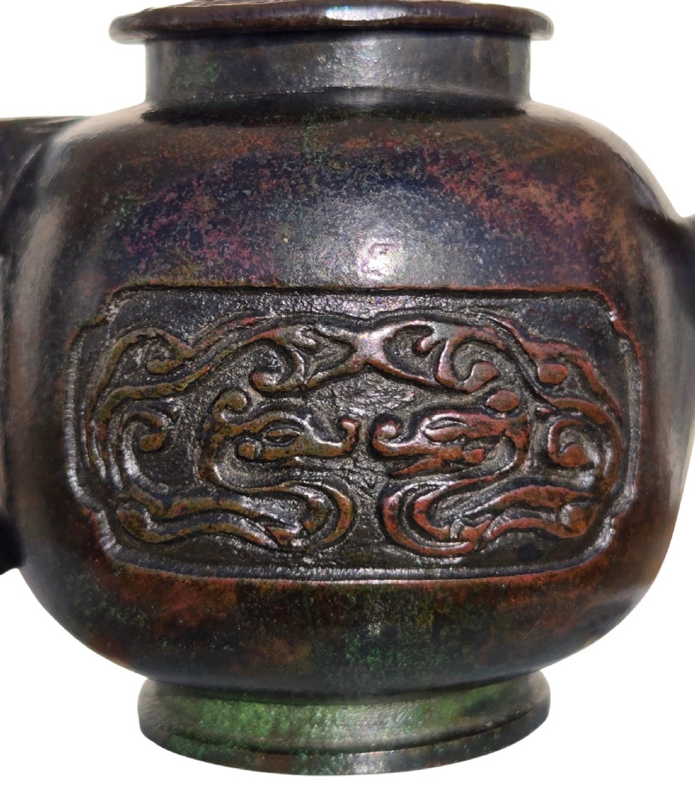 A dark patinated cast bronze vessel in ewer form featuring a dragon-head handle, a tapered spout, and carved relief panels. View VII