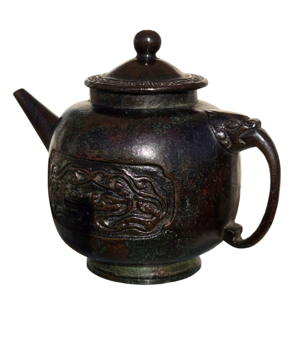 A dark patinated cast bronze vessel in ewer form featuring a dragon-head handle, a tapered spout, and carved relief panels. View IX