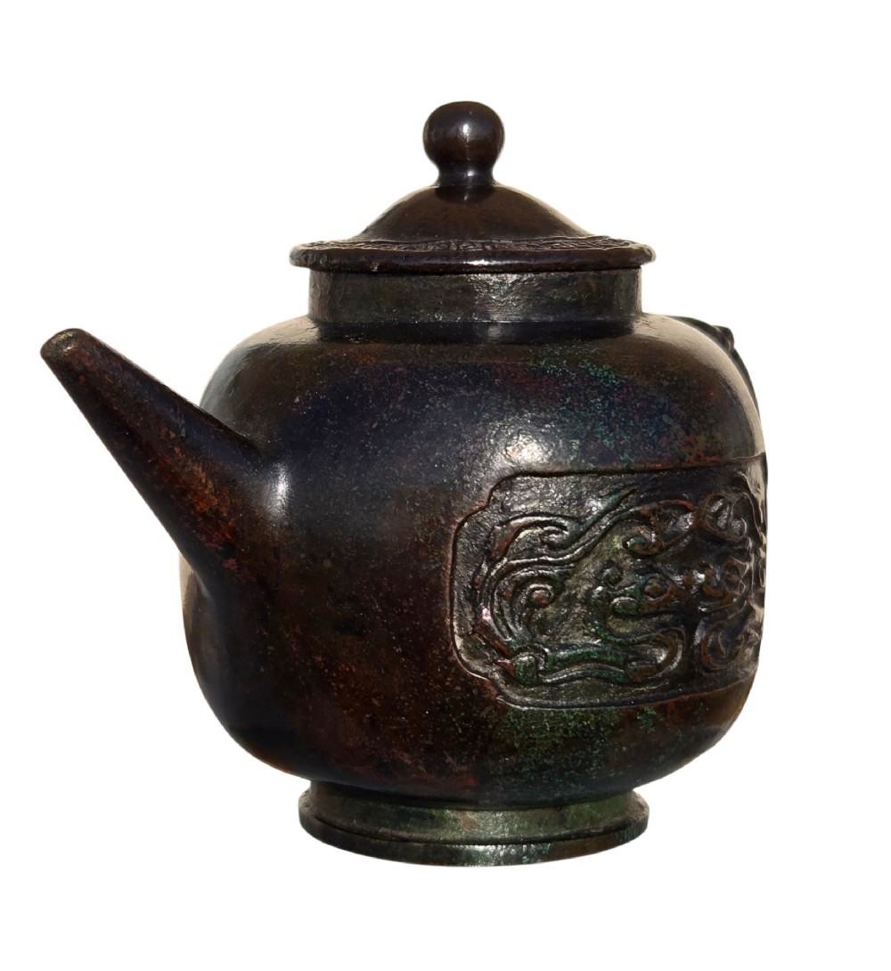 A dark patinated cast bronze vessel in ewer form featuring a dragon-head handle, a tapered spout, and carved relief panels. View X
