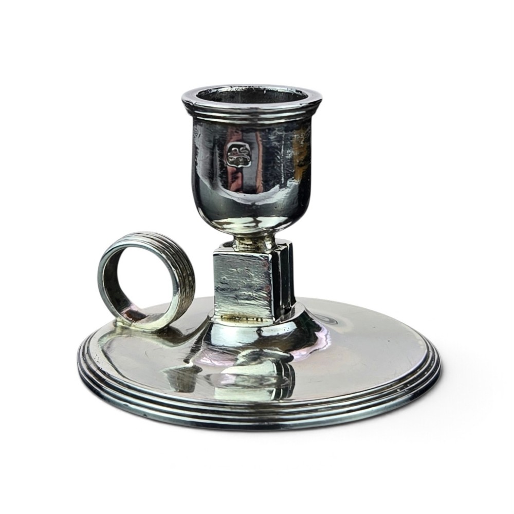 A small George III sterling silver taperstick featuring a flared sconce, a square central collar, a side ring handle, and a moulded circular base.
