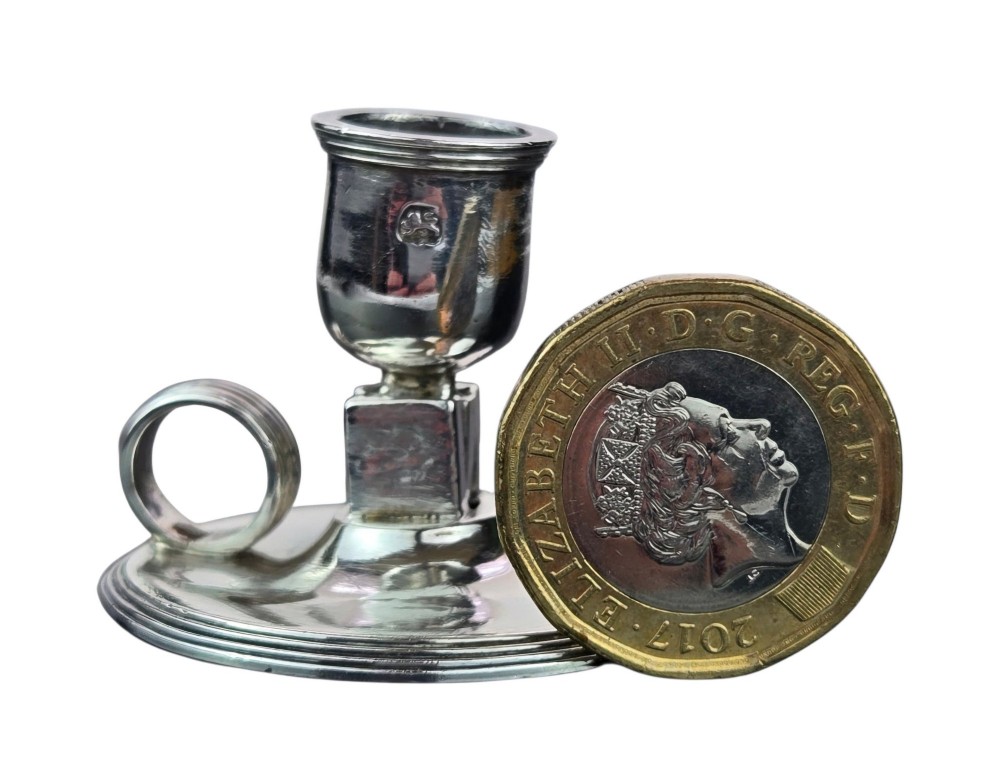 A small George III sterling silver taperstick featuring a flared sconce, a square central collar, a side ring handle, and a moulded circular base. View IV