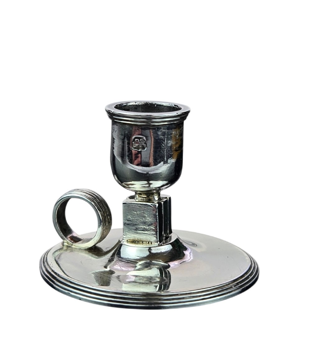 A small George III sterling silver taperstick featuring a flared sconce, a square central collar, a side ring handle, and a moulded circular base. View V