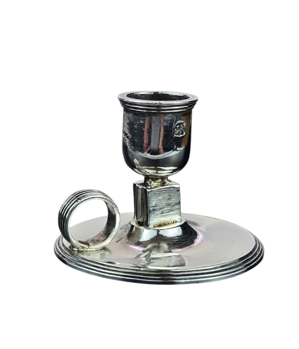 A small George III sterling silver taperstick featuring a flared sconce, a square central collar, a side ring handle, and a moulded circular base. View VI
