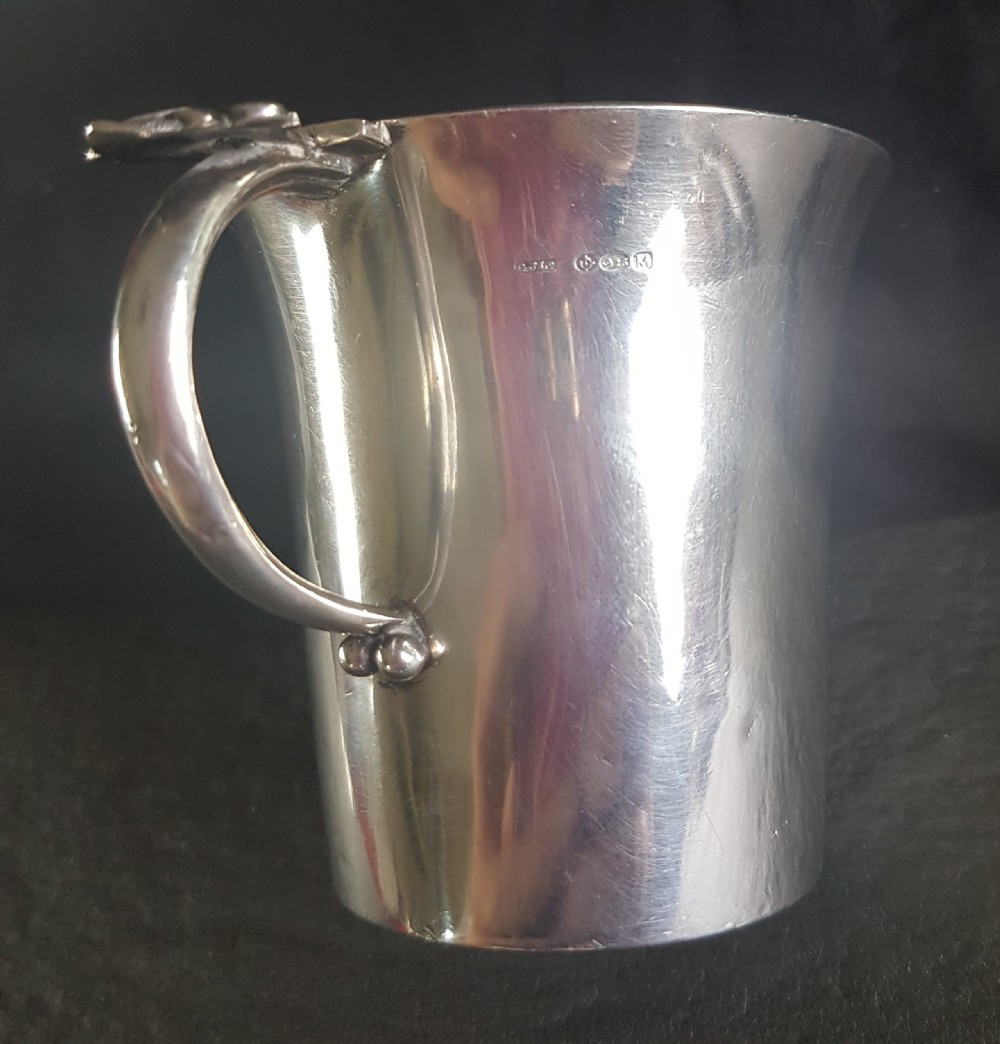 A sterling silver christening mug featuring a slightly flared rim, planished surface texture, and a curved loop handle detailed with an acorn motif. View II