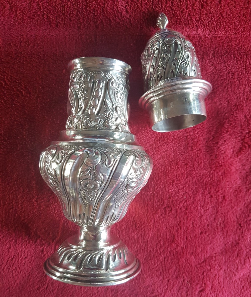 An ornate sterling silver sugar caster featuring intricate repousse floral motifs, a pierced decorative dome cover with a flame finial, and a fluted circular base. View II