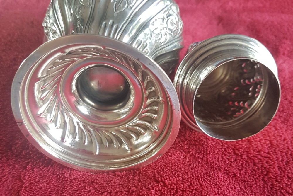 An ornate sterling silver sugar caster featuring intricate repousse floral motifs, a pierced decorative dome cover with a flame finial, and a fluted circular base. View III