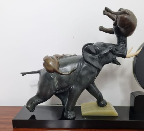 fig 1. An Art Deco mantel clock featuring a circular green onyx dial flanked by dark patinated spelter sculptures of an elephant and panthers on a layered marble base.