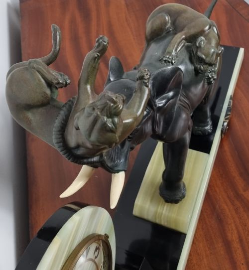 fig 2. An Art Deco mantel clock featuring a circular green onyx dial flanked by dark patinated spelter sculptures of an elephant and panthers on a layered marble base.