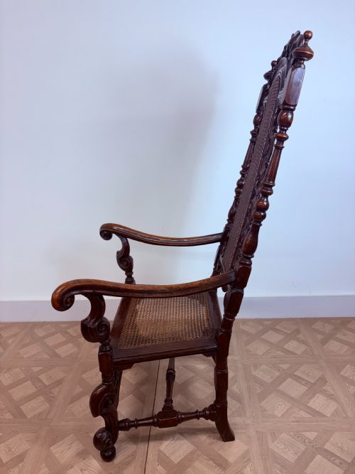 fig 1. A late 17th-century Carolean dark walnut armchair featuring an intricately carved cresting rail, high caned back panel, curved arms, and turned legs.
