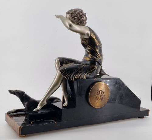 fig 3. An Art Deco mantel clock featuring a silvered metal figure of a seated woman flanked by two greyhounds atop a multi-coloured green and brown marble base with an octagonal dial.