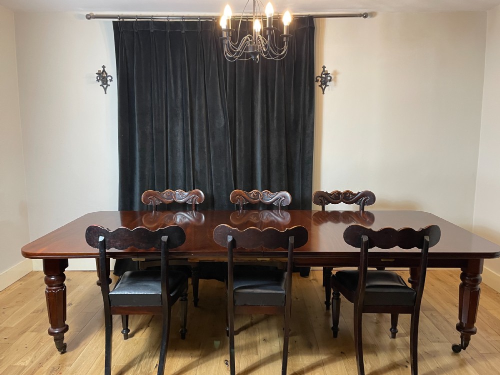 A William IV mahogany extending dining table with a polished surface, rounded corners, and turned reeded legs fitted with brass castors. View II