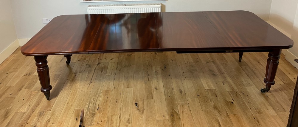 A William IV mahogany extending dining table with a polished surface, rounded corners, and turned reeded legs fitted with brass castors. View V