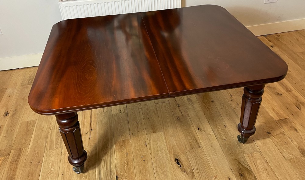A William IV mahogany extending dining table with a polished surface, rounded corners, and turned reeded legs fitted with brass castors. View VII