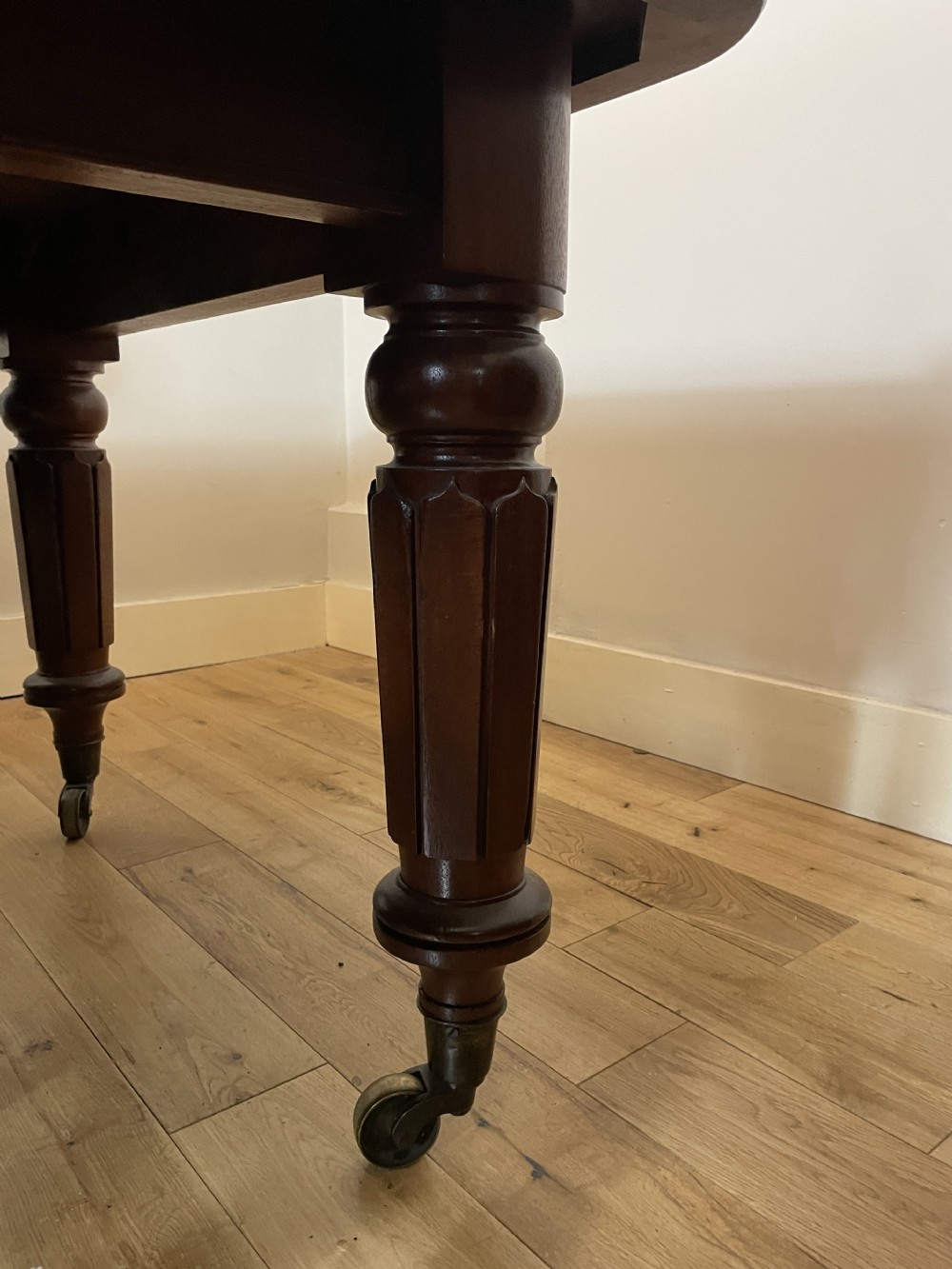 A William IV mahogany extending dining table with a polished surface, rounded corners, and turned reeded legs fitted with brass castors. View IX