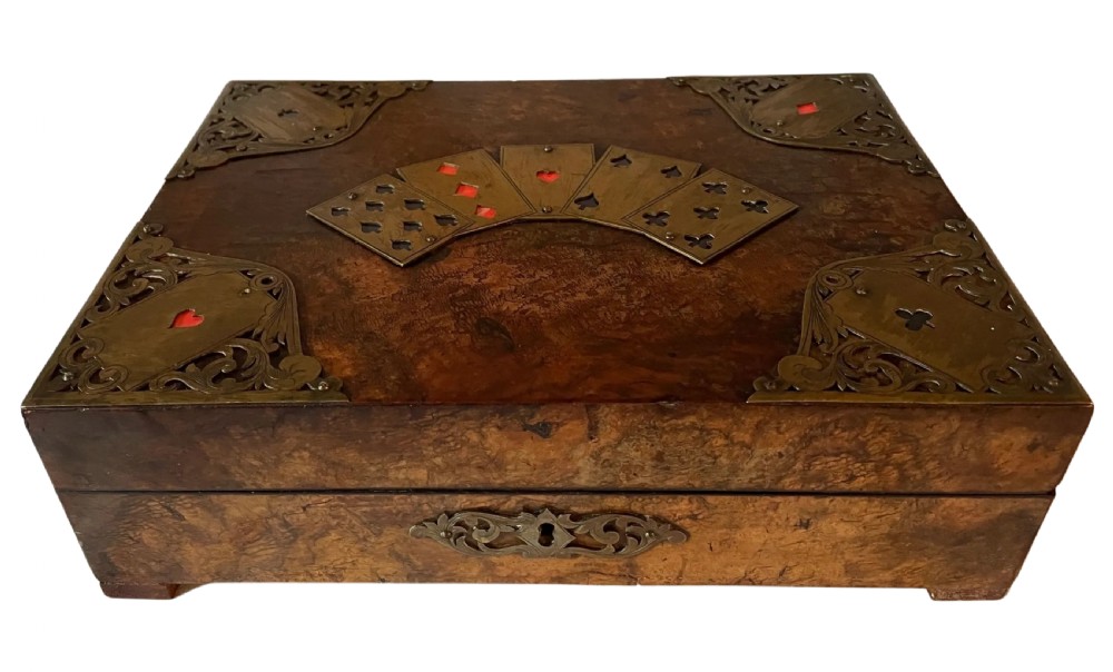 A rectangular Victorian burr walnut games box featuring decorative brass corner mounts shaped like playing cards and a fan-shaped brass playing card motif on the lid.