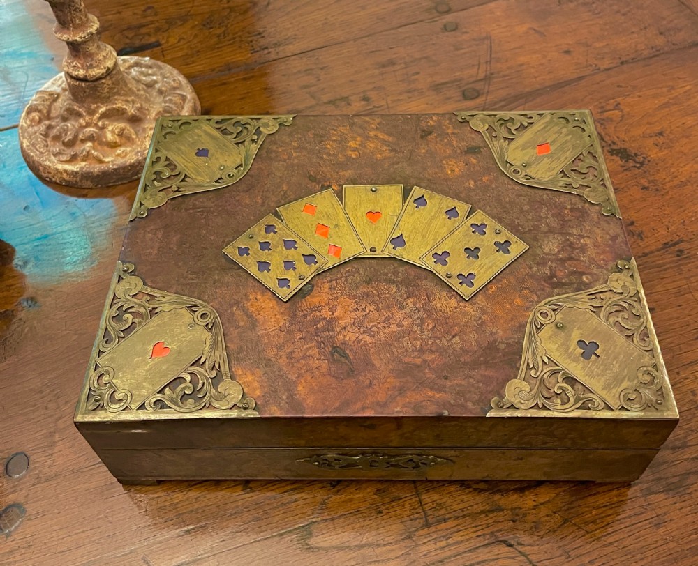 A rectangular Victorian burr walnut games box featuring decorative brass corner mounts shaped like playing cards and a fan-shaped brass playing card motif on the lid. View II