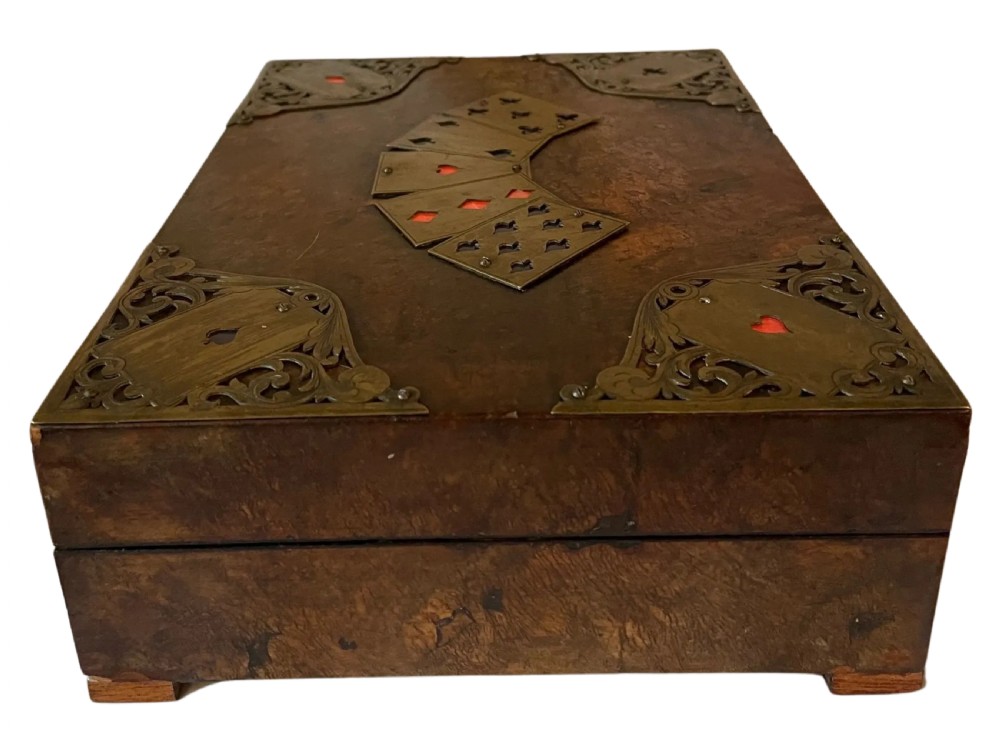 A rectangular Victorian burr walnut games box featuring decorative brass corner mounts shaped like playing cards and a fan-shaped brass playing card motif on the lid. View V