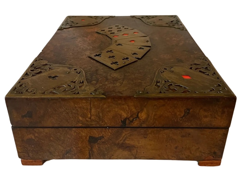 A rectangular Victorian burr walnut games box featuring decorative brass corner mounts shaped like playing cards and a fan-shaped brass playing card motif on the lid. View VI