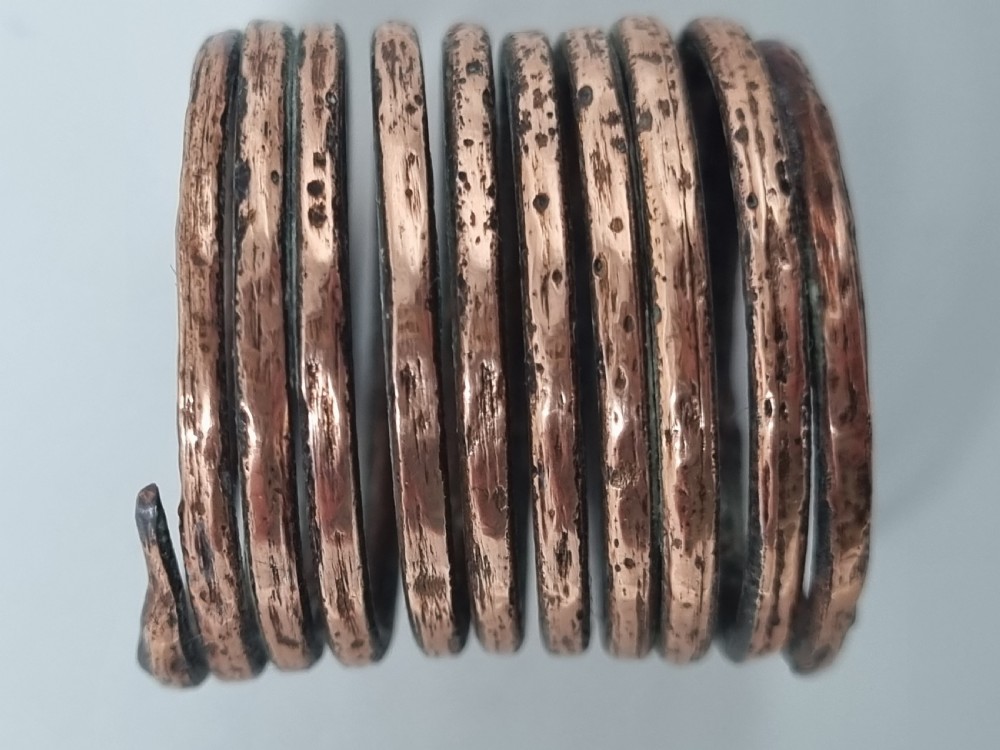 An ancient bronze ring crafted from a continuous coiled metal spiral with a textured, patinated surface. View V