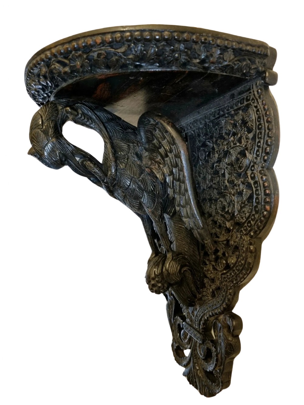 A 19th-century dark carved teak wall bracket featuring an undercut bird support figure and intricate foliate tracery.