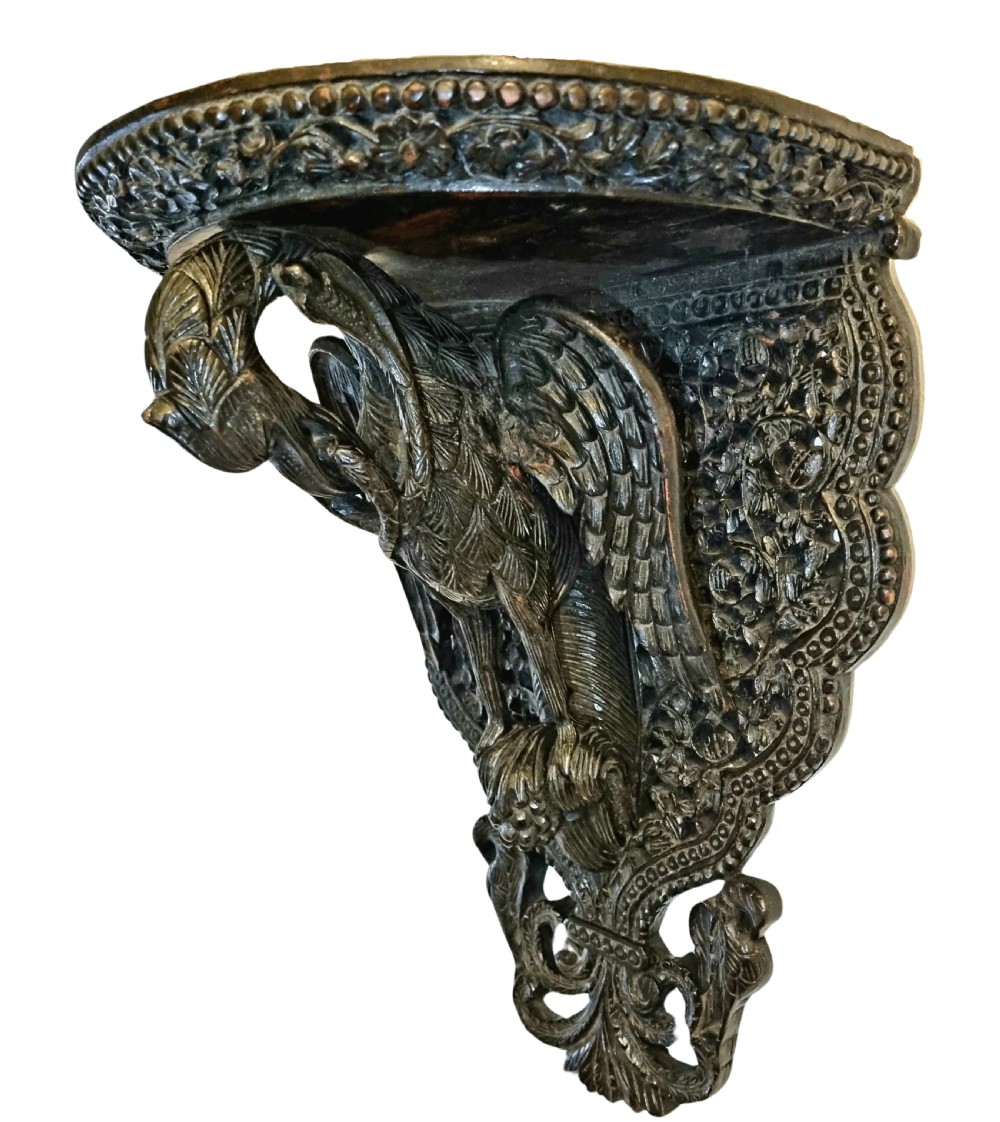 A 19th-century dark carved teak wall bracket featuring an undercut bird support figure and intricate foliate tracery. View V