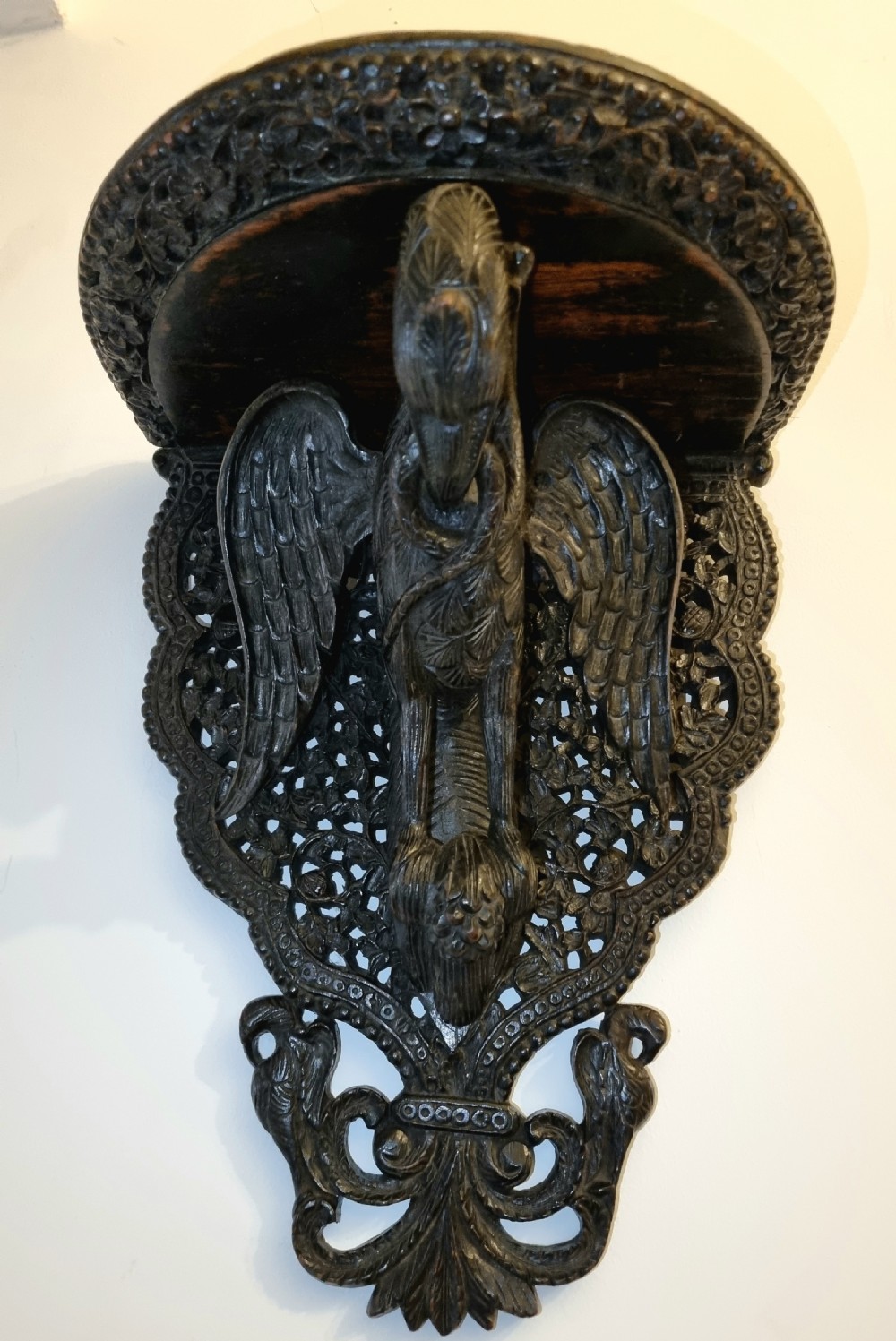 A 19th-century dark carved teak wall bracket featuring an undercut bird support figure and intricate foliate tracery. View VI