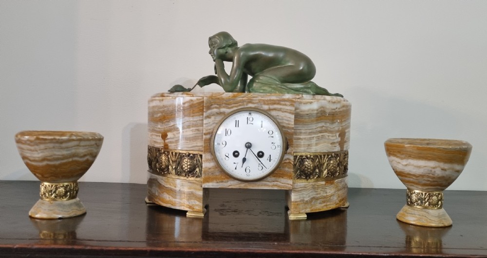 An Art Deco clock garniture set featuring a carved onyx mantel clock topped with a green patinated bronze sculpture of a kneeling woman, accompanied by two matching onyx cups. View IV