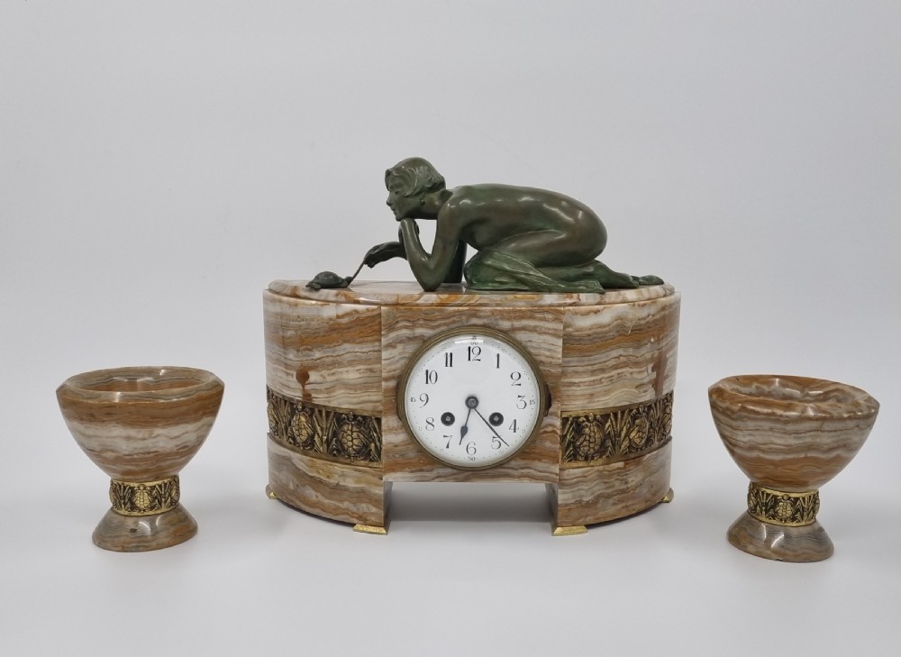 An Art Deco clock garniture set featuring a carved onyx mantel clock topped with a green patinated bronze sculpture of a kneeling woman, accompanied by two matching onyx cups. View XIII