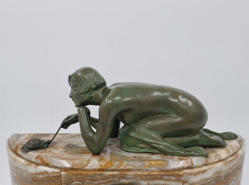An Art Deco clock garniture set featuring a carved onyx mantel clock topped with a green patinated bronze sculpture of a kneeling woman, accompanied by two matching onyx cups. View XV