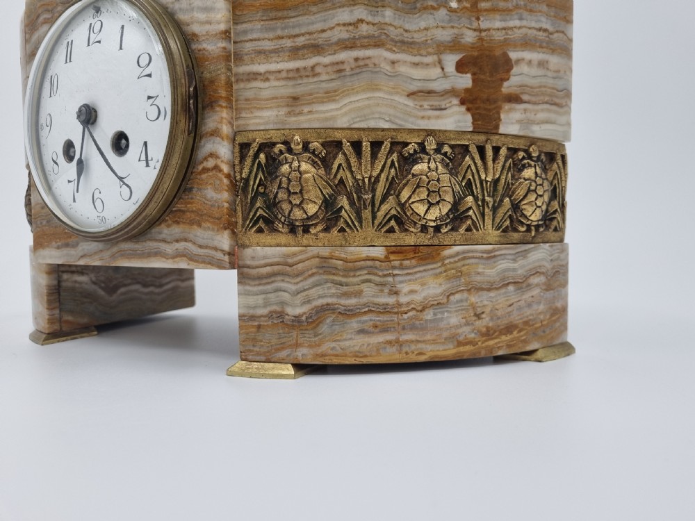 An Art Deco clock garniture set featuring a carved onyx mantel clock topped with a green patinated bronze sculpture of a kneeling woman, accompanied by two matching onyx cups. View XVII