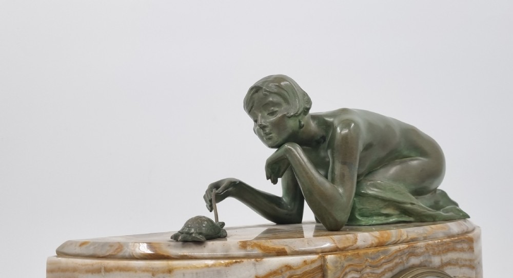 An Art Deco clock garniture set featuring a carved onyx mantel clock topped with a green patinated bronze sculpture of a kneeling woman, accompanied by two matching onyx cups. View XVIII