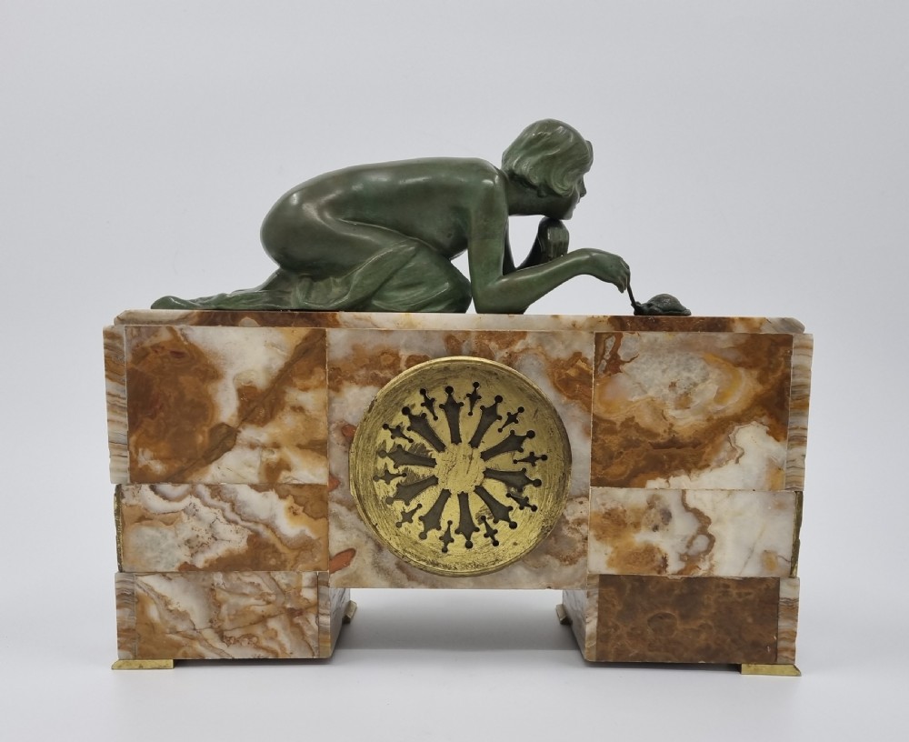 An Art Deco clock garniture set featuring a carved onyx mantel clock topped with a green patinated bronze sculpture of a kneeling woman, accompanied by two matching onyx cups. View XIX