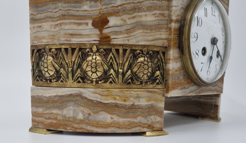 An Art Deco clock garniture set featuring a carved onyx mantel clock topped with a green patinated bronze sculpture of a kneeling woman, accompanied by two matching onyx cups. View XX