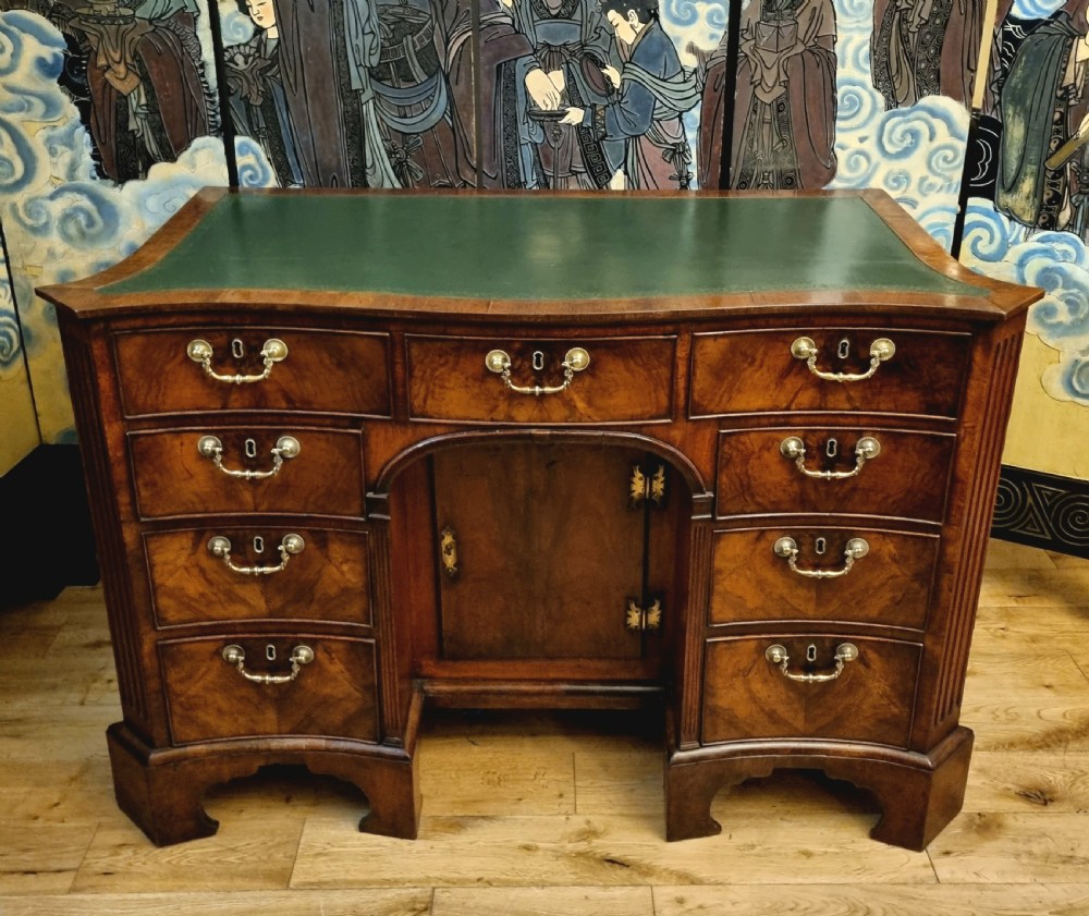 An 18th-century mahogany kneehole desk featuring a serpentine front, green leather inset top, brass hardware, and a central recessed cupboard. View II
