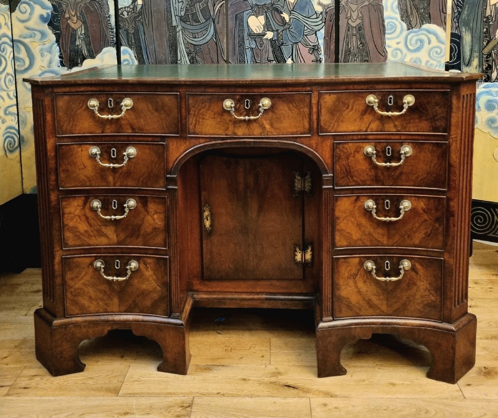 An 18th-century mahogany kneehole desk featuring a serpentine front, green leather inset top, brass hardware, and a central recessed cupboard. View III