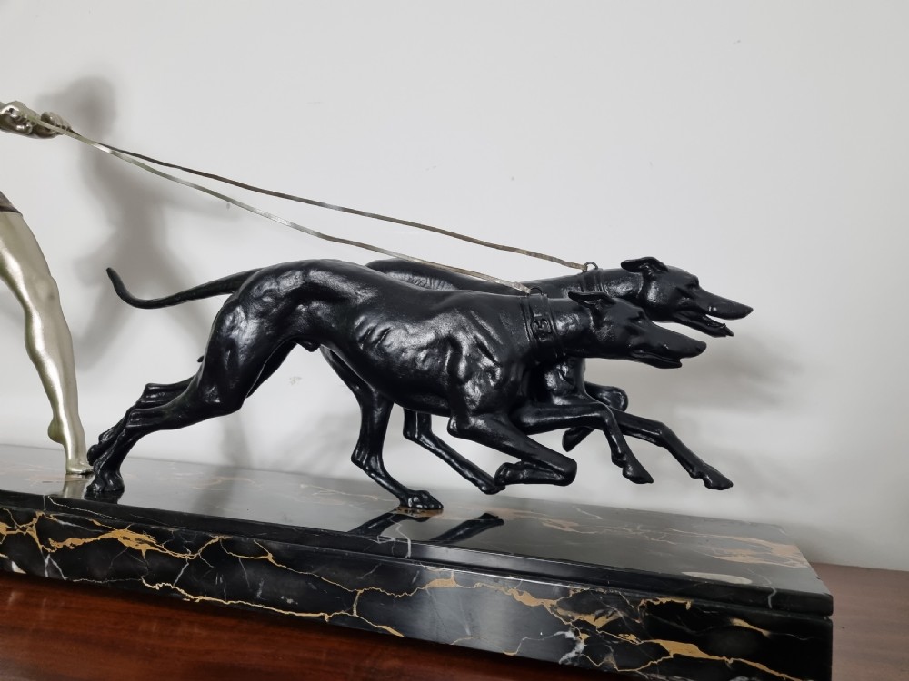 An Art Deco sculpture depicting a silvered female figure running alongside two dark greyhounds, mounted on a black marble base. View III