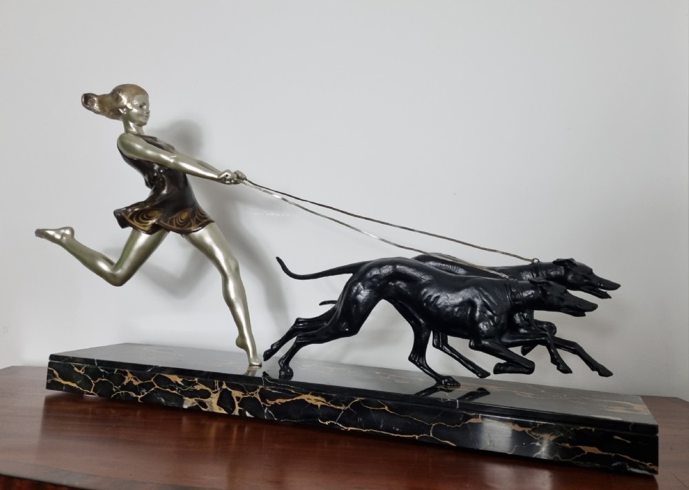 An Art Deco sculpture depicting a silvered female figure running alongside two dark greyhounds, mounted on a black marble base. View IV