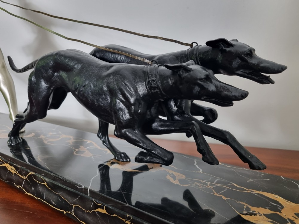 An Art Deco sculpture depicting a silvered female figure running alongside two dark greyhounds, mounted on a black marble base. View VI
