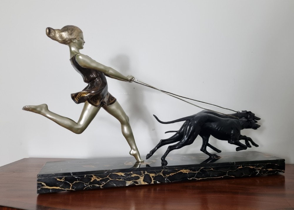 An Art Deco sculpture depicting a silvered female figure running alongside two dark greyhounds, mounted on a black marble base. View VII